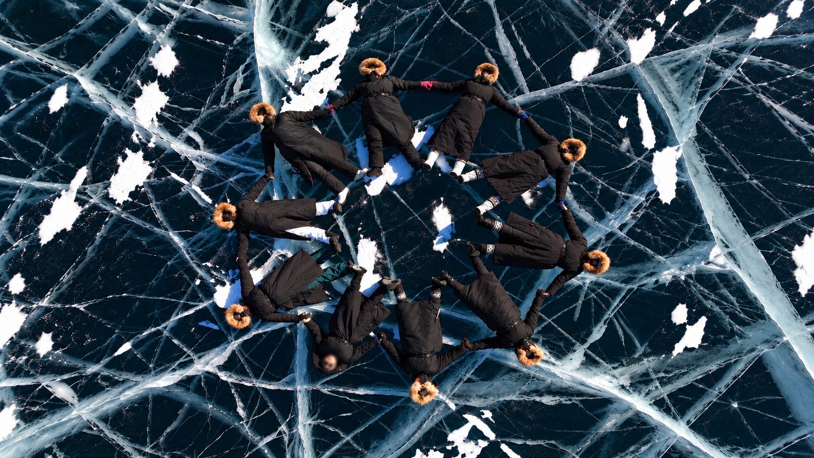 Women lying in a star shape on cracked lake ice, seen from above