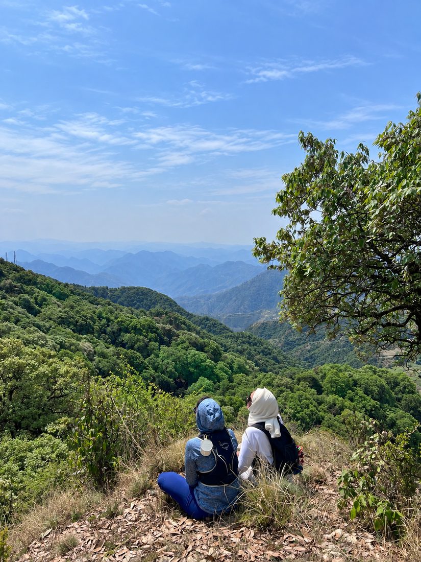 Two women sitting on a hillside above a valley of misty mountains